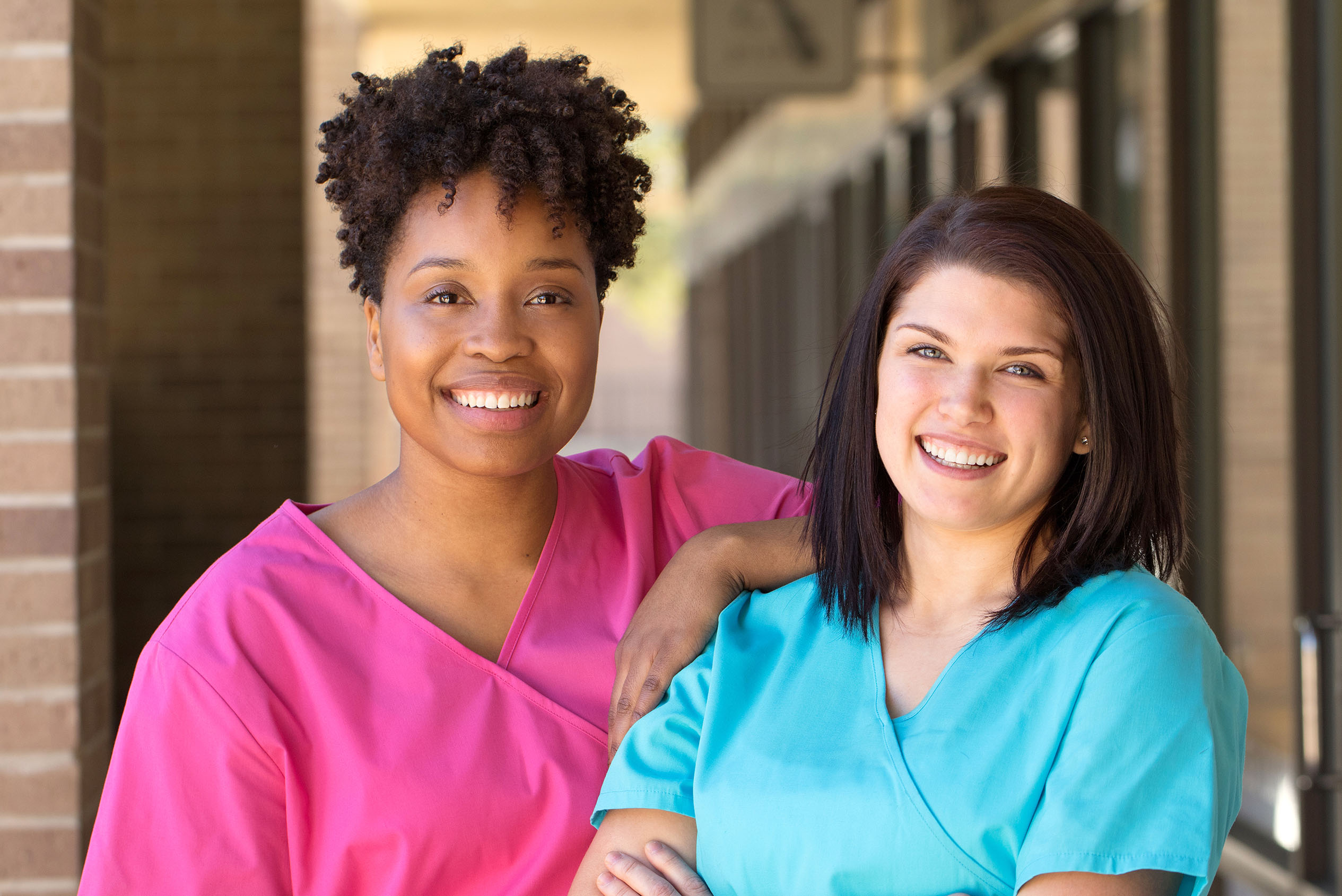 2 women outside hospital wearing scrubs and smiling