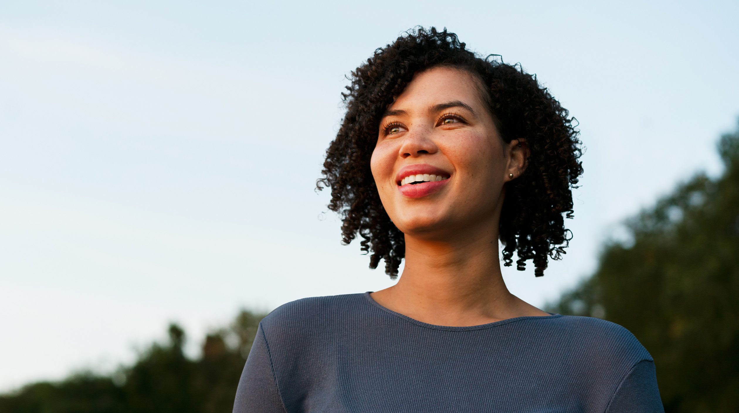 Female standing outside staring off and smiling