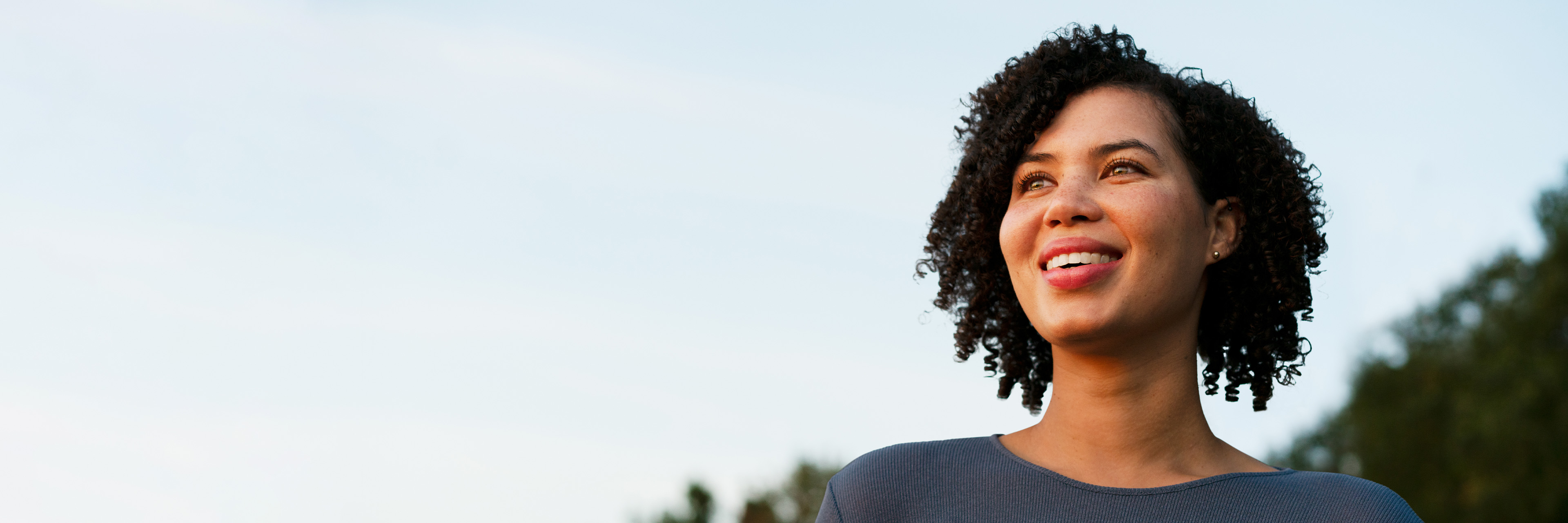 Female standing outside staring off and smiling
