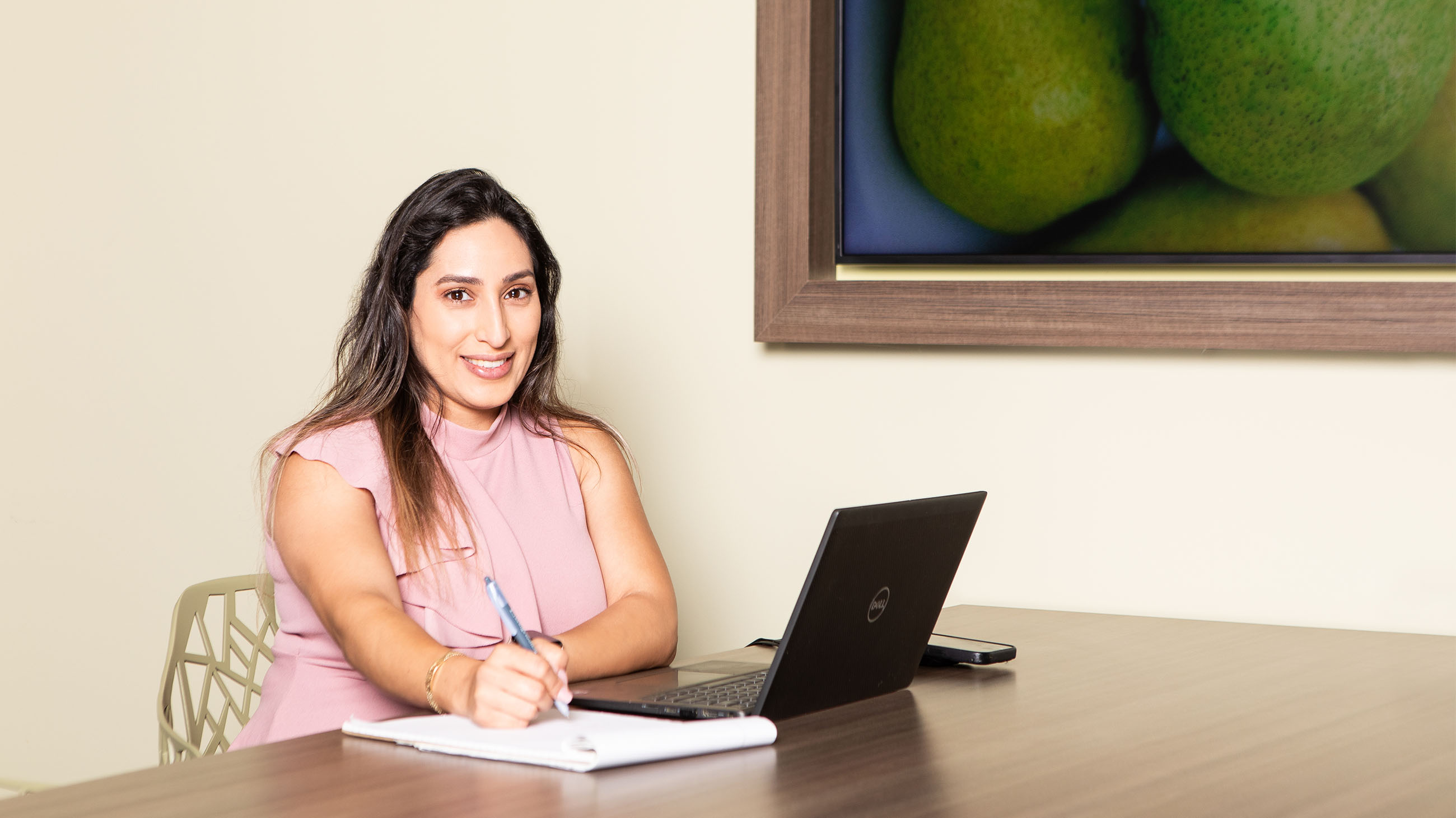 woman writing on notepad in front of laptop