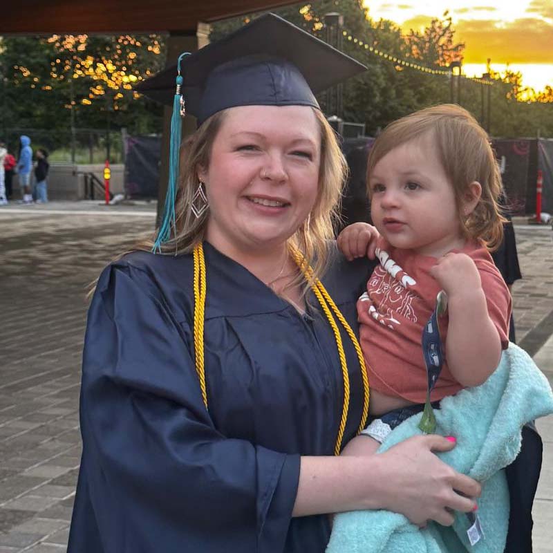 woman wearing graduation cap smiling and holding toddler